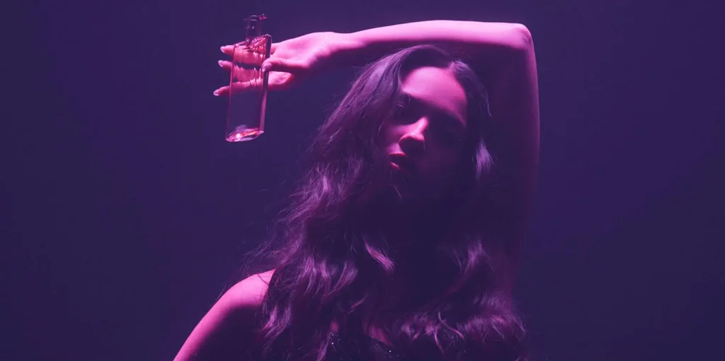 Олівія Родріго під рожевим світлом тримає флакон Idole Power eau de parfum Intense